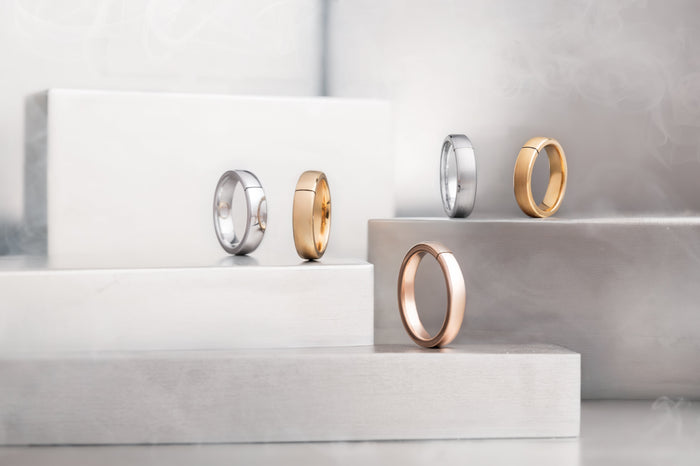 Cinque anelli di pagamento NFC in argento, oro giallo e oro rosa su piedistalli geometrici bianchi; gioielli tecnologici miPAGO accessibili e inclusivi