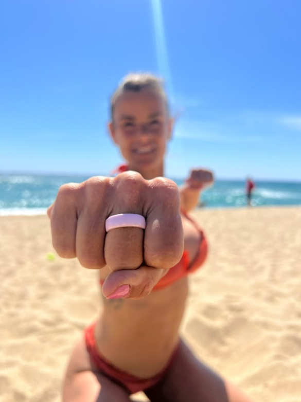 Donna in spiaggia con PAGO Ring rosa al dito in pugno verso la fotocamera anello di pagamento NFC per le vacanze estive